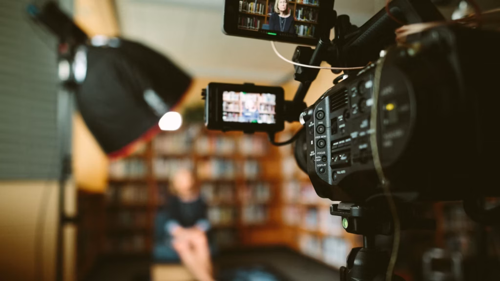 A woman sits on a stool in a library in front of a camera, filming an interview that she hopes will become the next viral real estate video