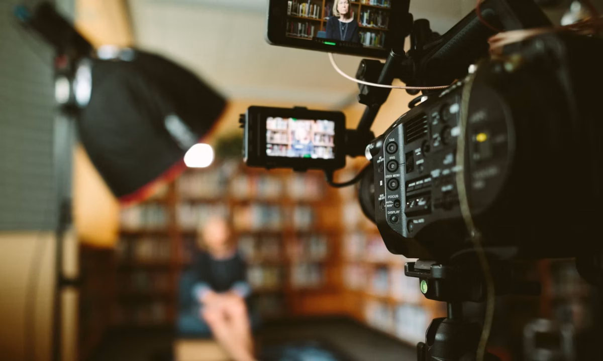 A woman sits on a stool in a library in front of a camera, filming an interview that she hopes will become the next viral real estate video
