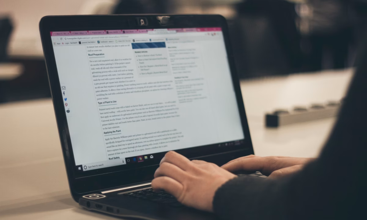 Woman in black sits in front of black laptop typing up a real estate blog entry about roofing