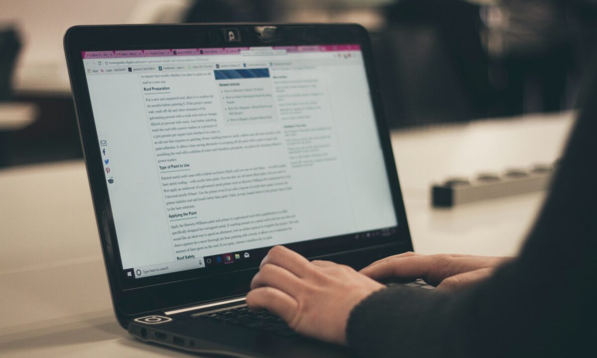 Woman in black sits in front of black laptop typing up a real estate blog entry about roofing