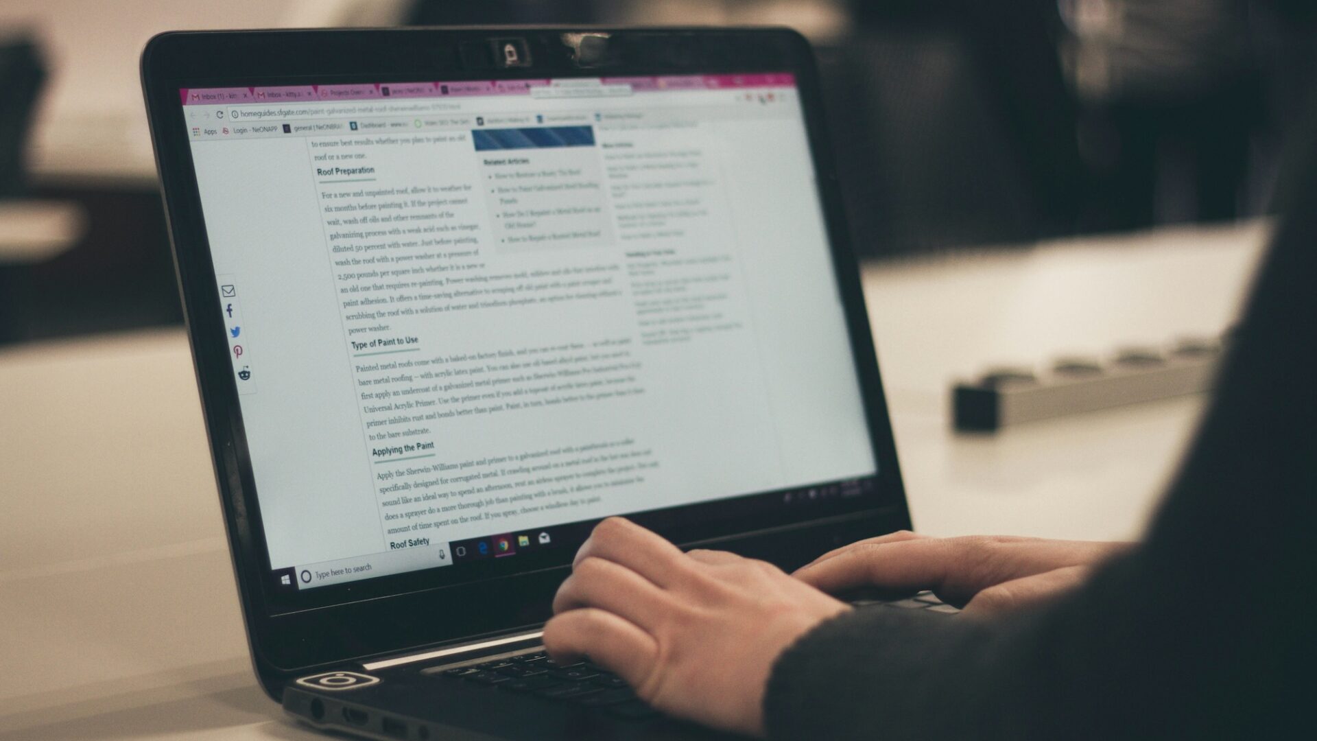 Woman in black sits in front of black laptop typing up a real estate blog entry about roofing