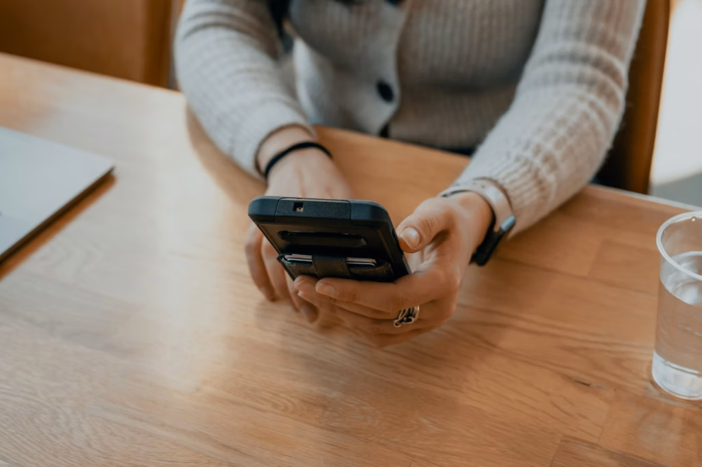 Person sits at wooden desk typing out a message to a real estate chatbot on their smartphone