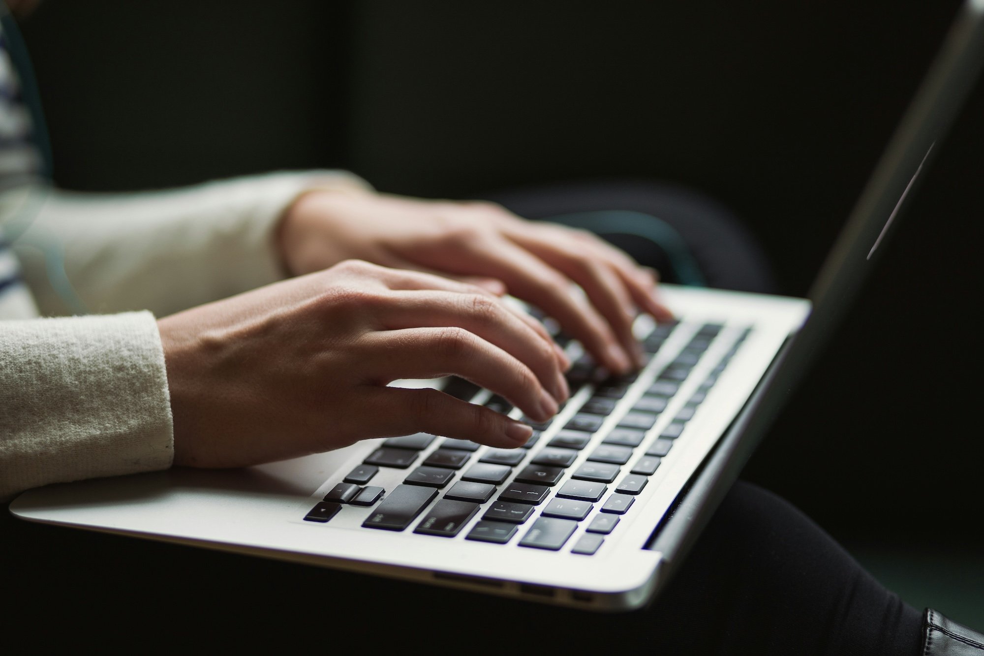 Close up of hands with white sweater typing on laptop