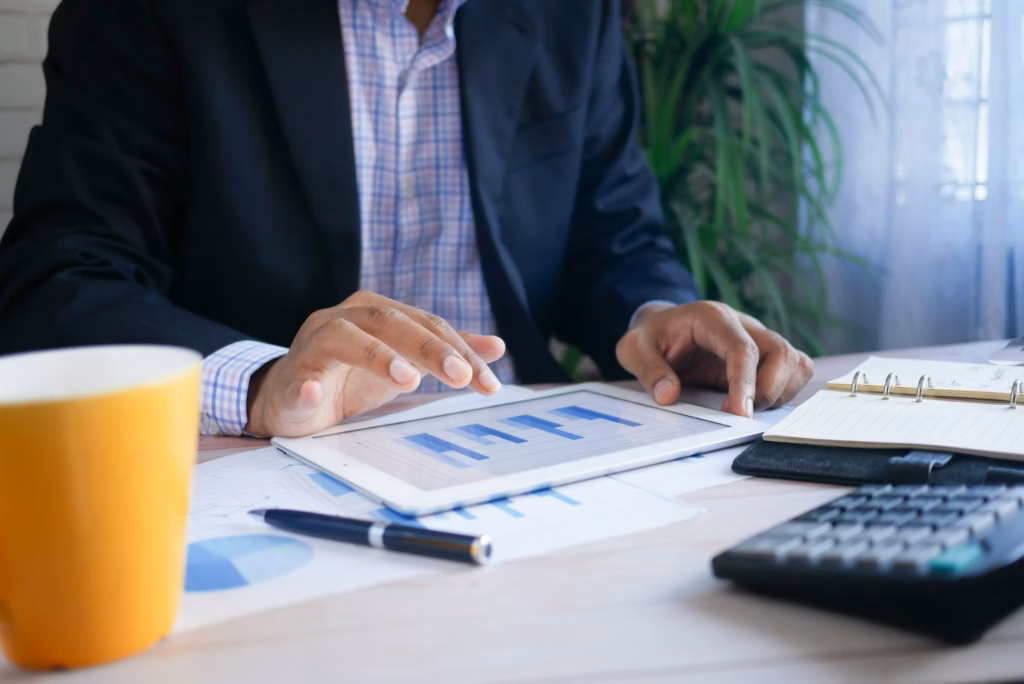 Real estate agent figuring out expenses at a desk with a calculator, tablet and cup of coffee in front of him