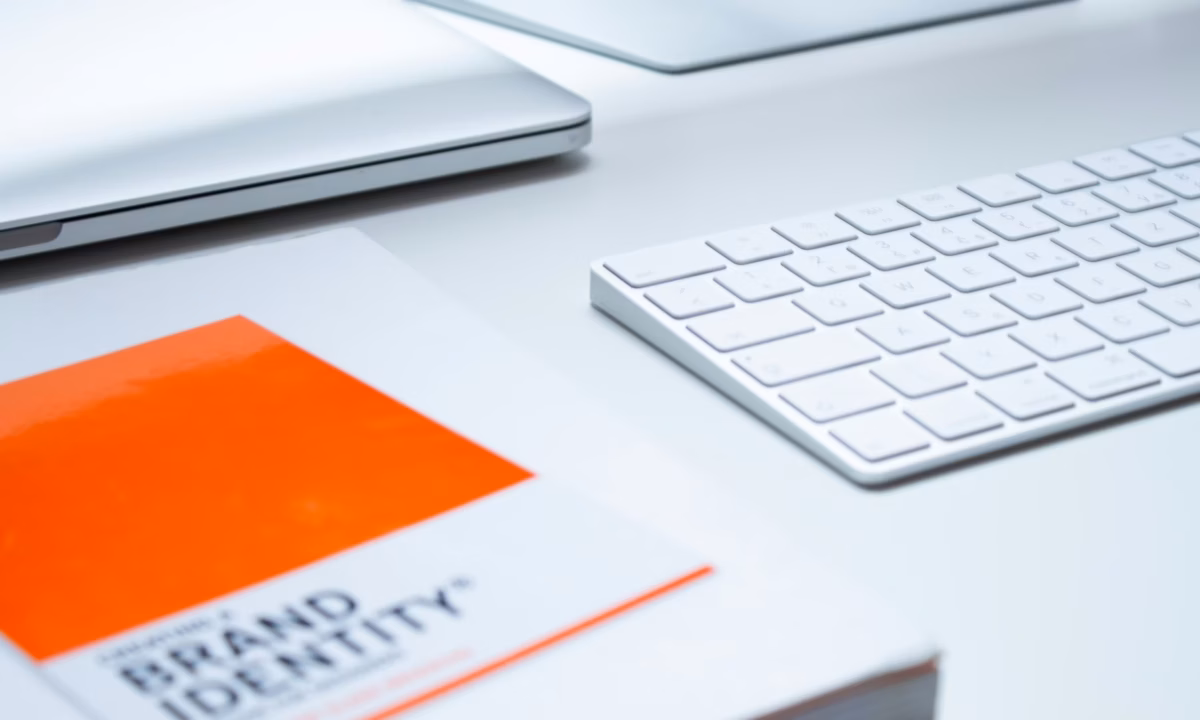 Keyboard, laptop and brand identity book sit on a white desk of a real estate agent looking to build a brand identity