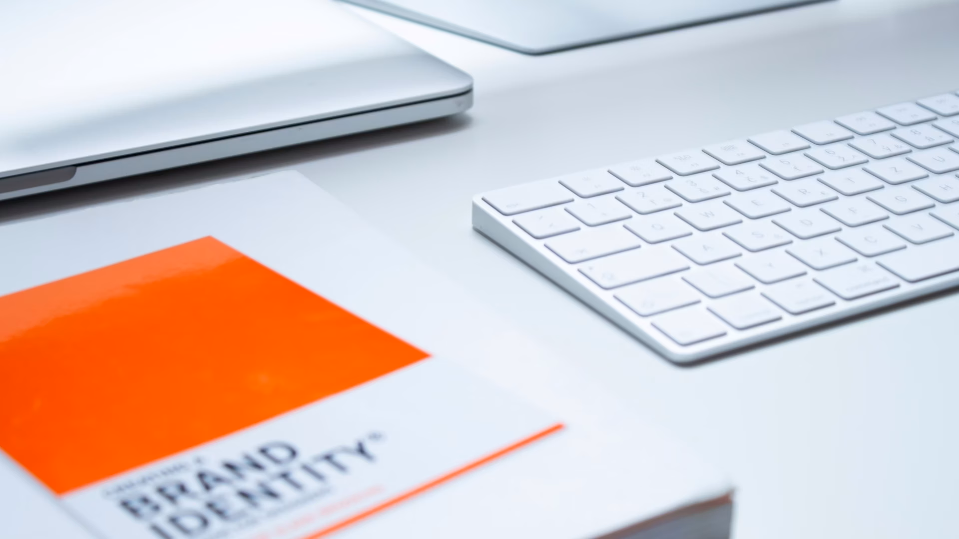 Keyboard, laptop and brand identity book sit on a white desk of a real estate agent looking to build a brand identity