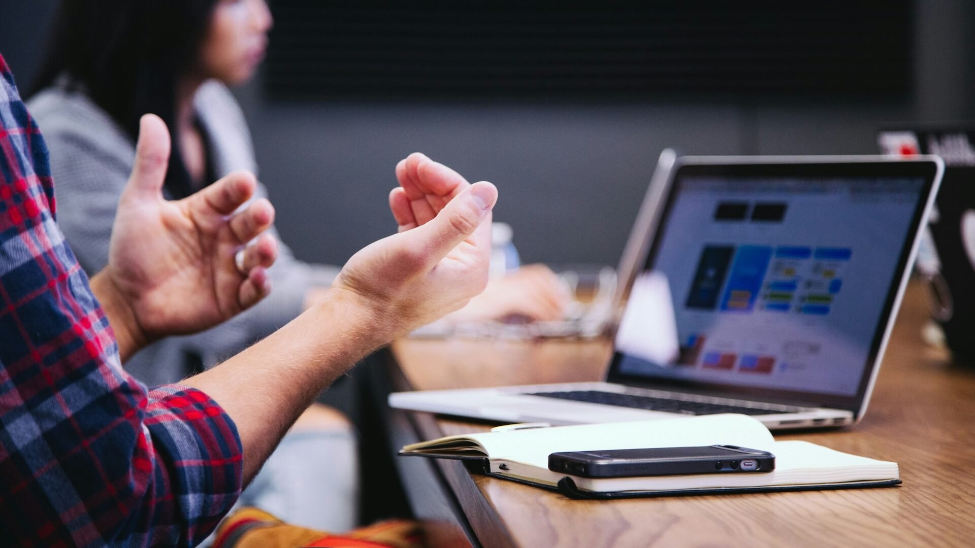 Two real estate agents sit at a wooden table in front of a laptop, notebook and smartphone discussing the merits of choosing between Agent Image vs Luxury Presence for their website and marketing needs