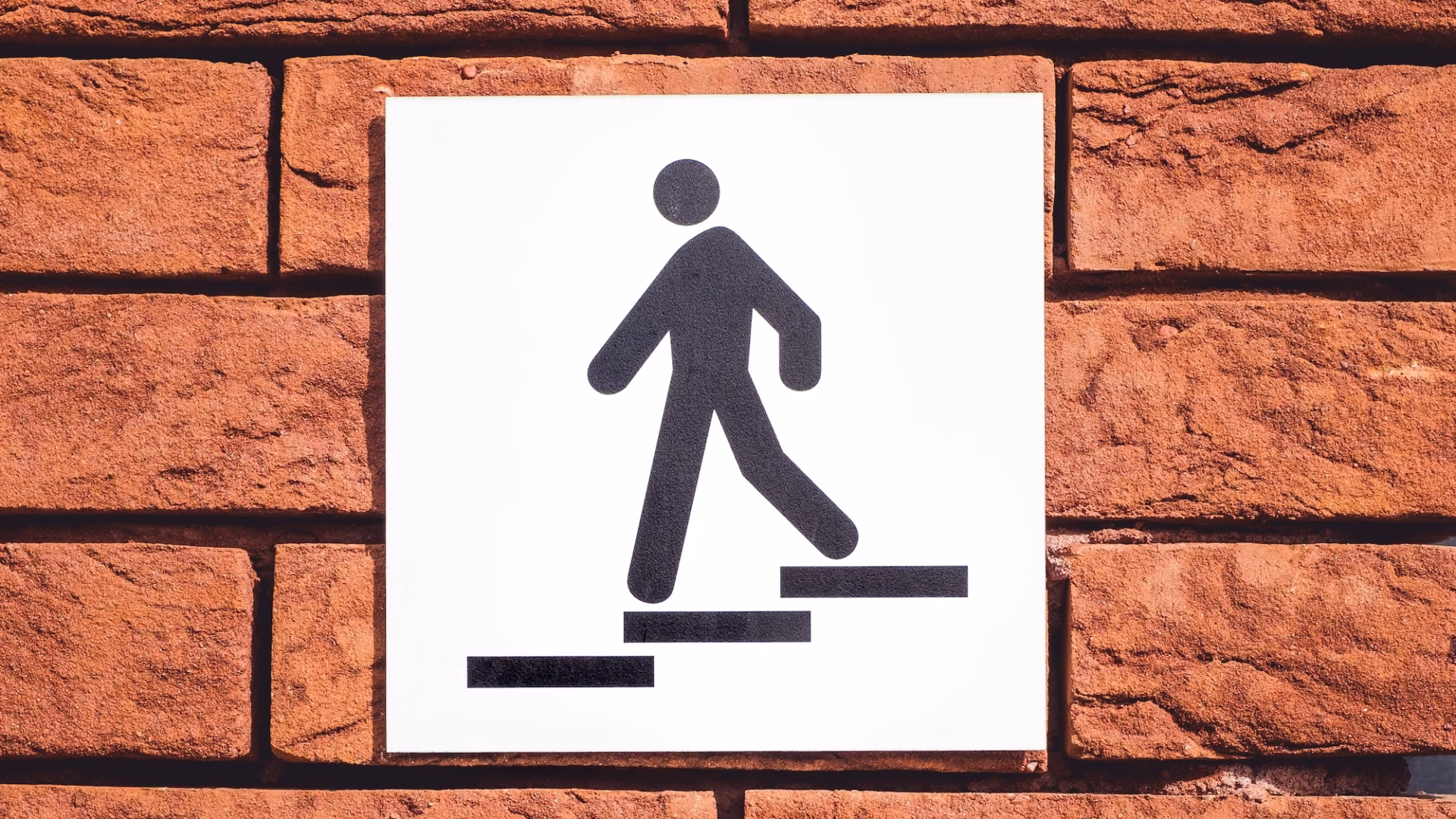 A sign on a brick wall showing a figure descending stairs as a metaphor for real estate lead magnets helping prospects move down the sales funnel