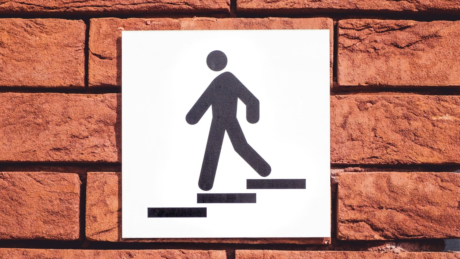 A sign on a brick wall showing a figure descending stairs as a metaphor for real estate lead magnets helping prospects move down the sales funnel