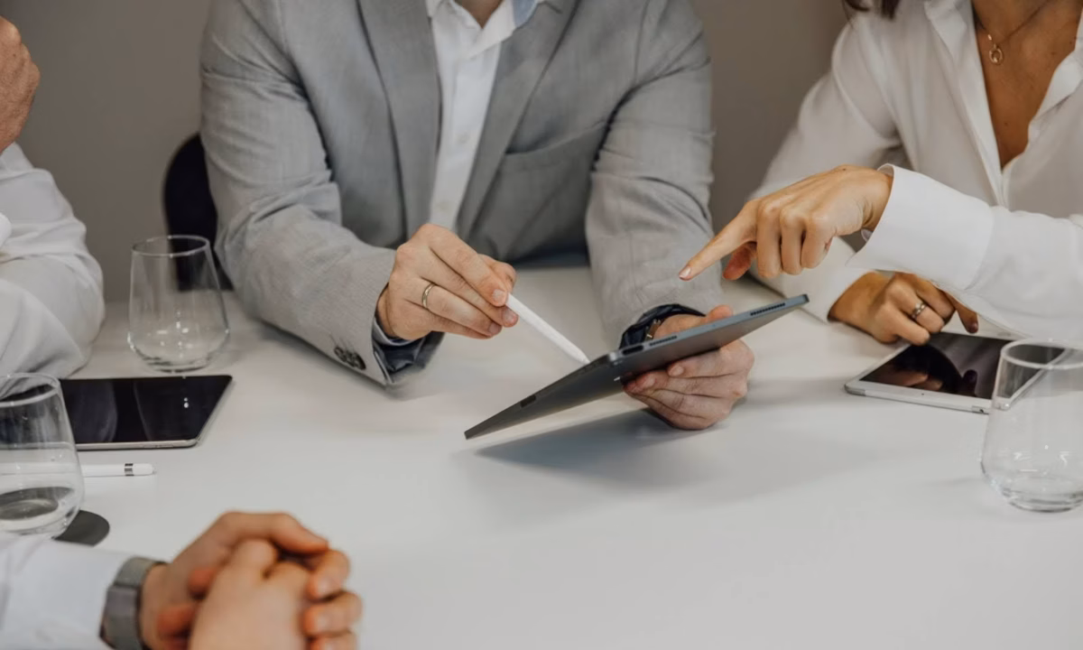 A real estate agent sits with clients pointing to a tablet with a stylus, demonstrating a client-centric approach