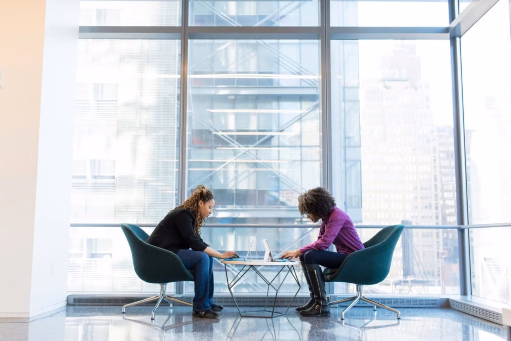 Two real estate agents sit facing each other in front of a floor to ceiling window, representing dual agency
