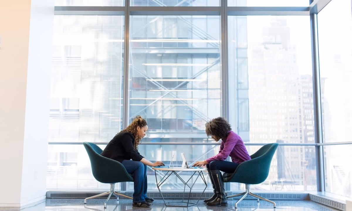 Two real estate agents sit facing each other in front of a floor to ceiling window, representing dual agency