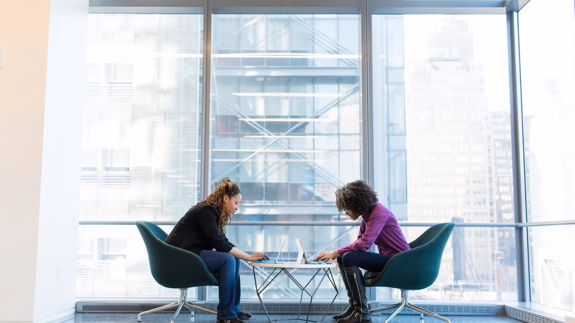 Two real estate agents sit facing each other in front of a floor to ceiling window, representing dual agency