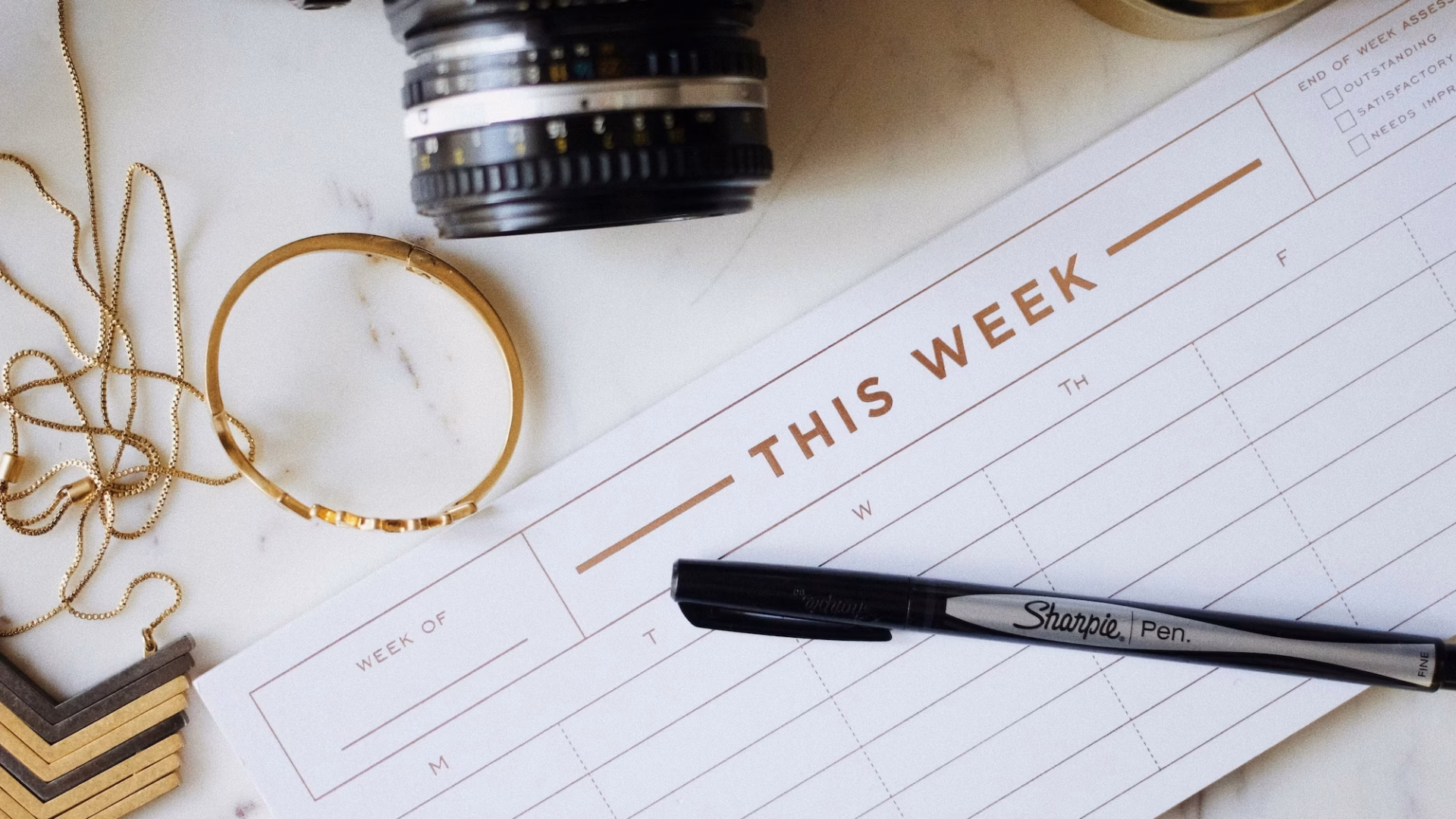 desk with jewelry, a camera and a social media content calendar headlined with "this week"