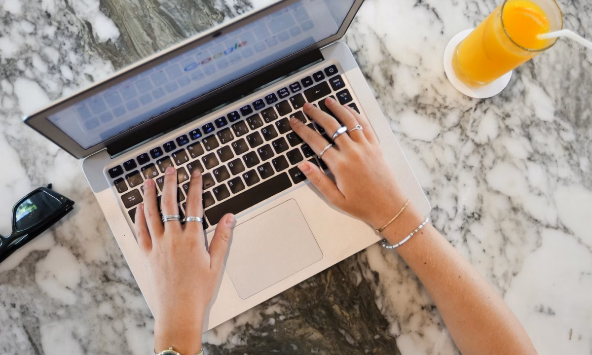 Real estate agent at marble desk with glass of orange juice next to them types of laptop working to Create google business profile