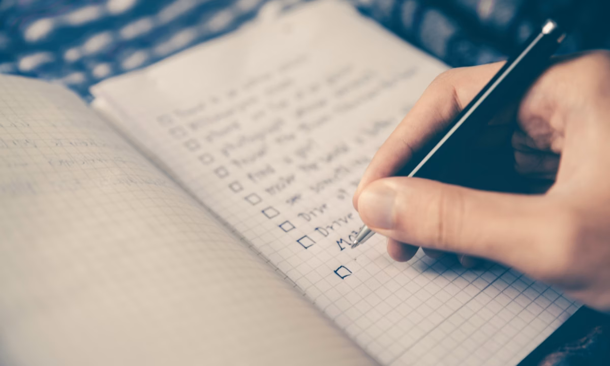 Hand writing in a journal with checkboxes, representing a person working on strategic marketing goals in real estate