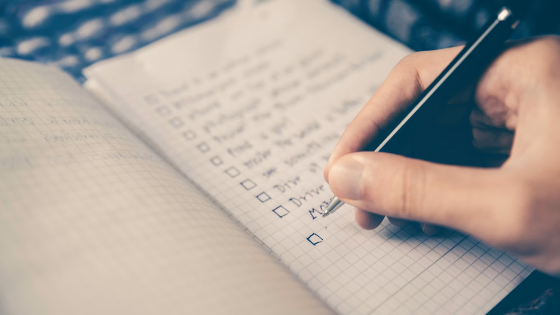 Hand writing in a journal with checkboxes, representing a person working on strategic marketing goals in real estate