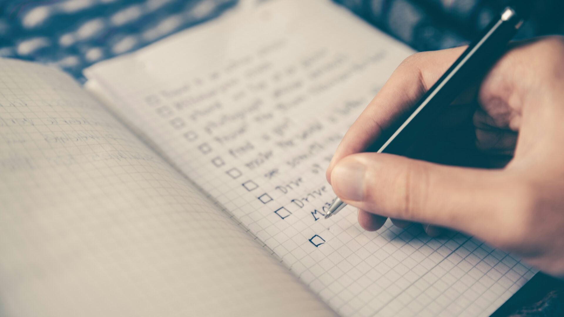 Hand writing in a journal with checkboxes, representing a person working on strategic marketing goals in real estate