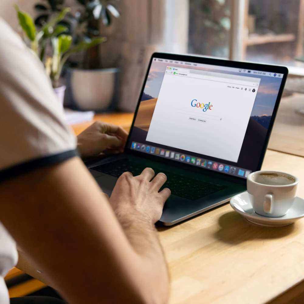 A person sits in front of an empty coffee cup and a laptop with Google's search page open on the screen to illustrate the need to grow your google business profile audience as a real estate agent