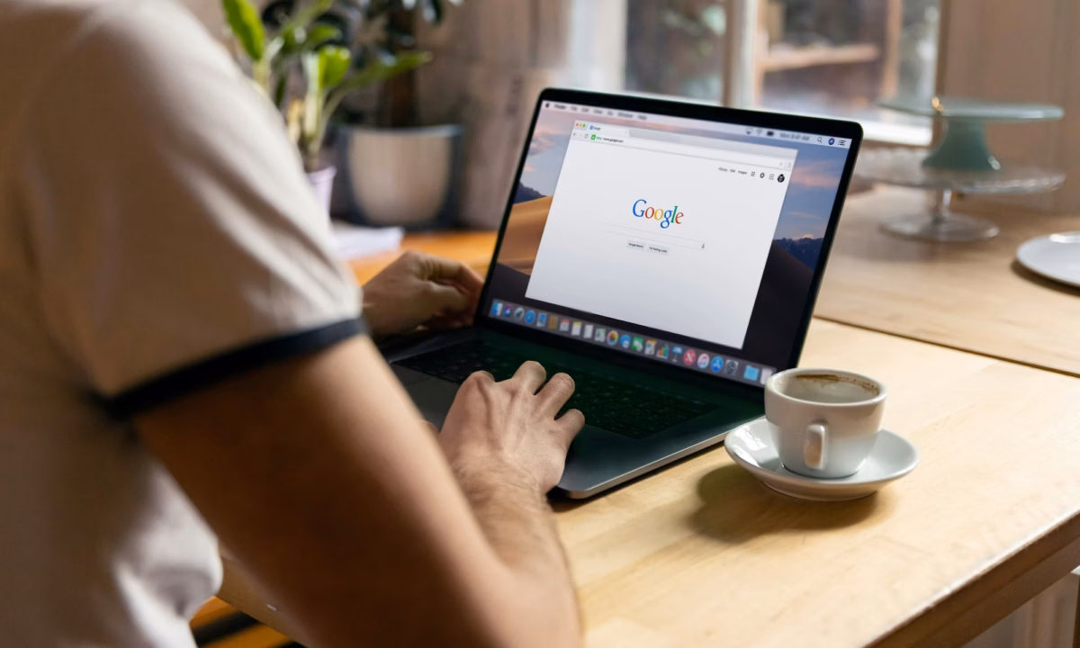 A person sits in front of an empty coffee cup and a laptop with Google's search page open on the screen to illustrate the need to grow your google business profile audience as a real estate agent