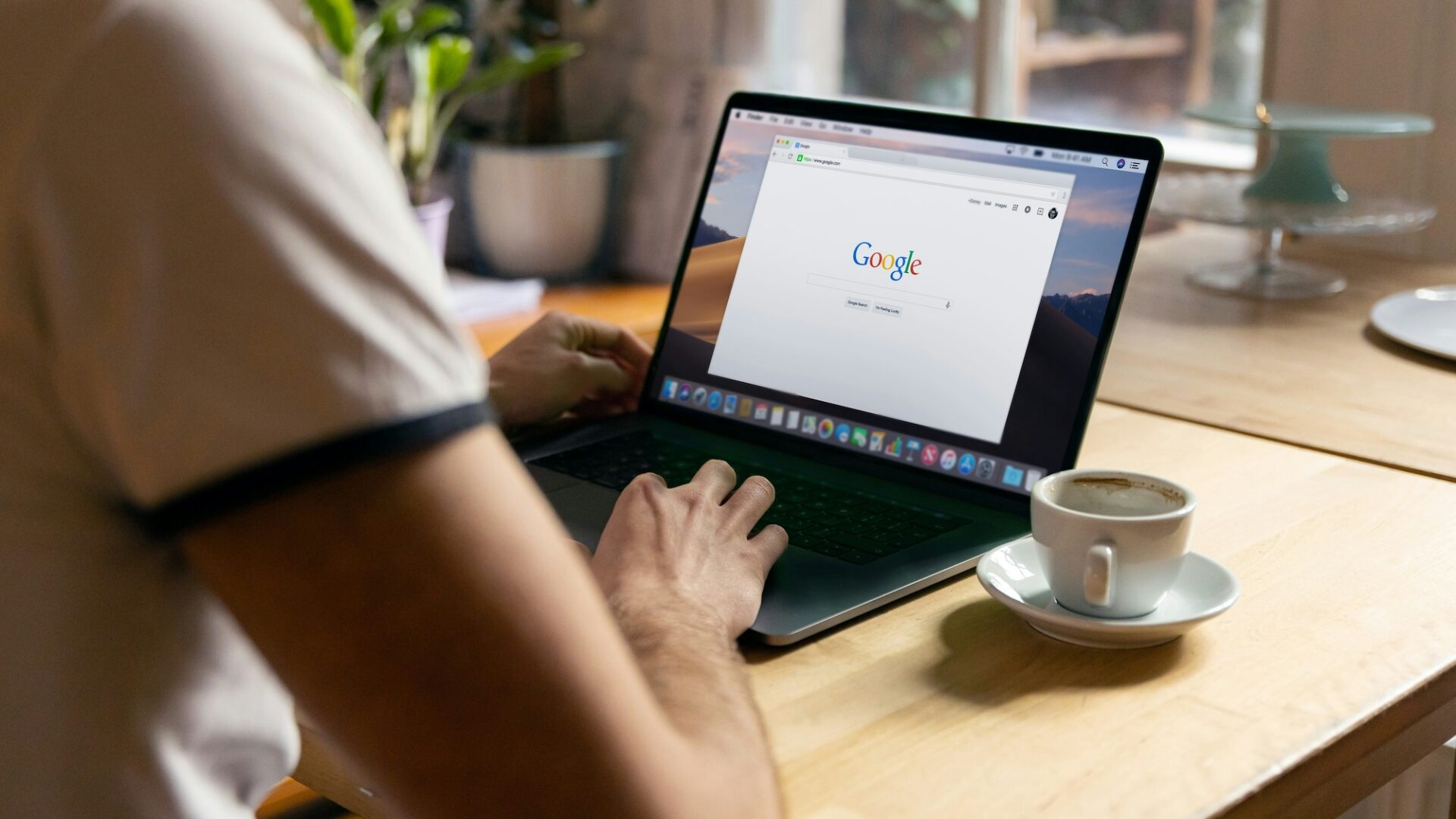 A person sits in front of an empty coffee cup and a laptop with Google's search page open on the screen to illustrate the need to grow your google business profile audience as a real estate agent