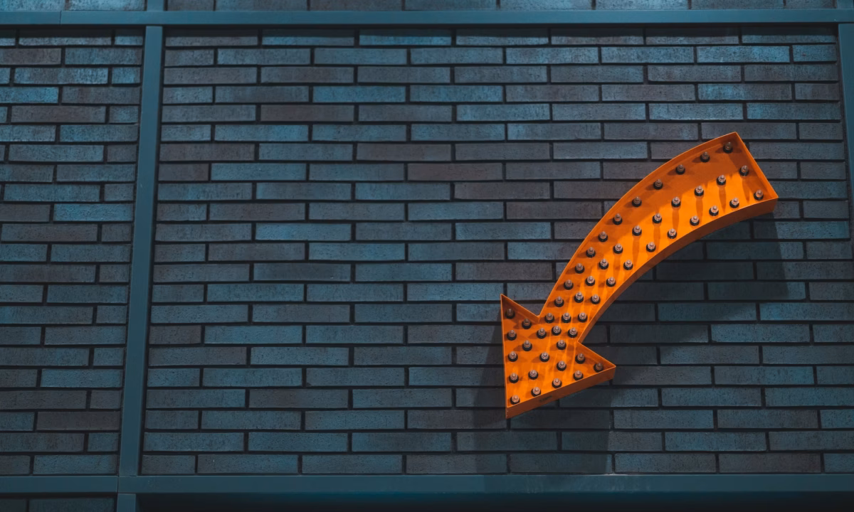 An orange arrow with lightbulbs in it on a brick wall, representing a Real estate CTA