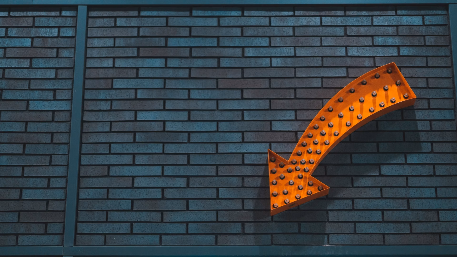 An orange arrow with lightbulbs in it on a brick wall, representing a Real estate CTA