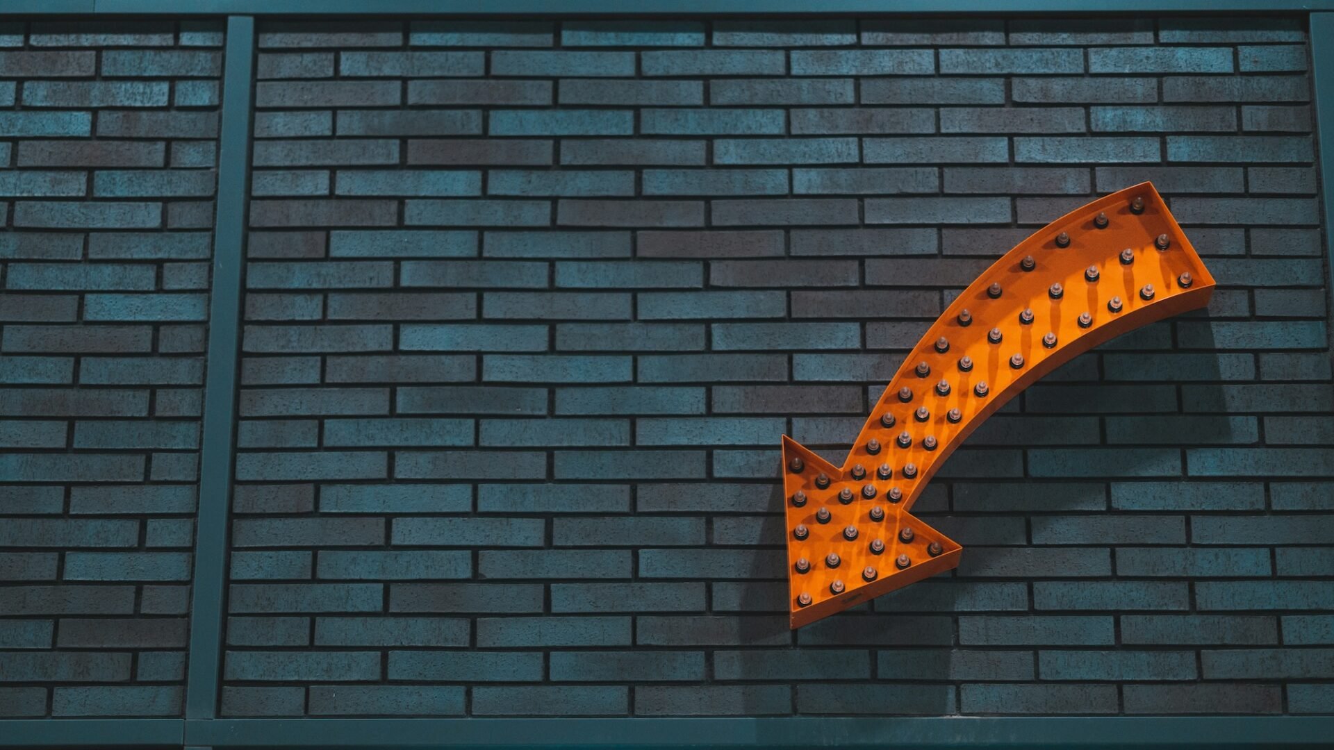 An orange arrow with lightbulbs in it on a brick wall, representing a Real estate CTA