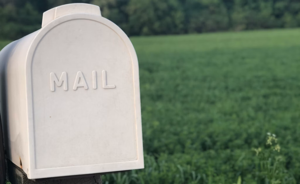 A cream colored mailbox with the word "mail" on it standing in front of a grassy expanse