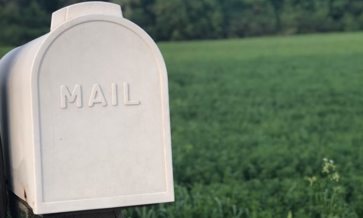 A cream colored mailbox with the word "mail" on it standing in front of a grassy expanse