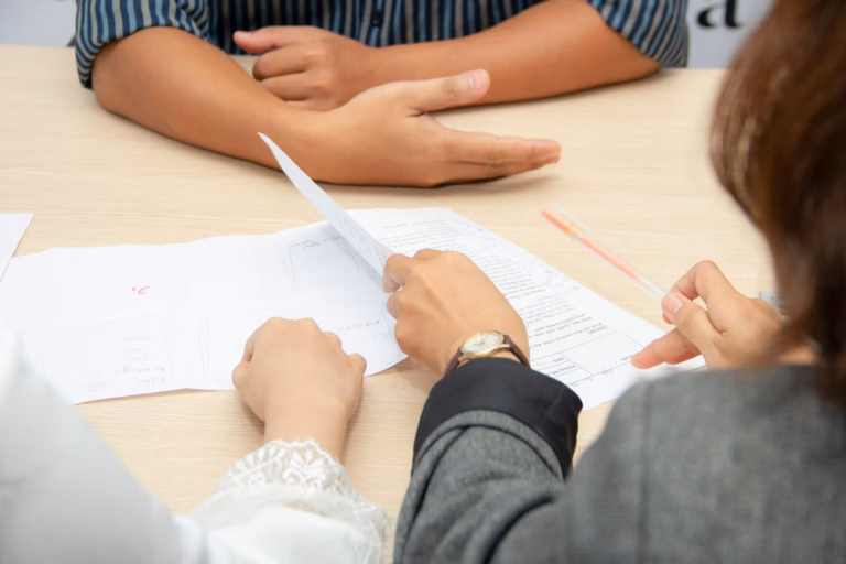 Two people look through a real estate agent resume at a desk with another person across from them
