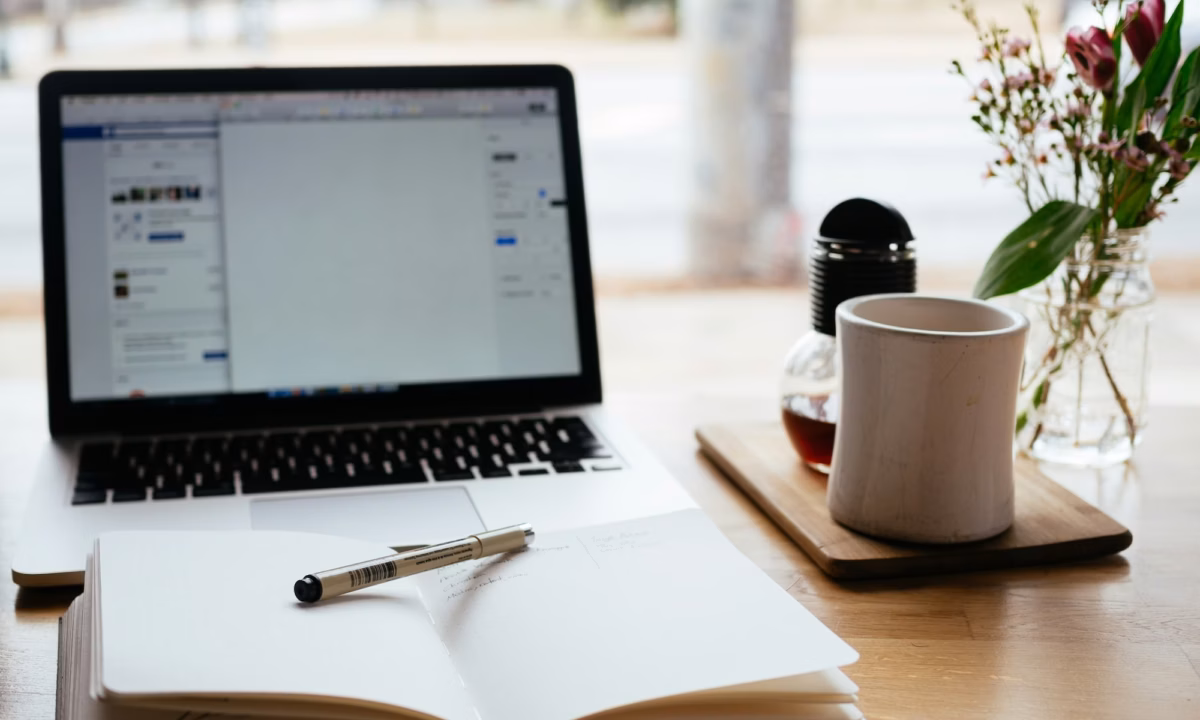 Notebook with marketing terminology written in it, with pen laid across it, sits on a desk in front of a laptop and cup of coffee