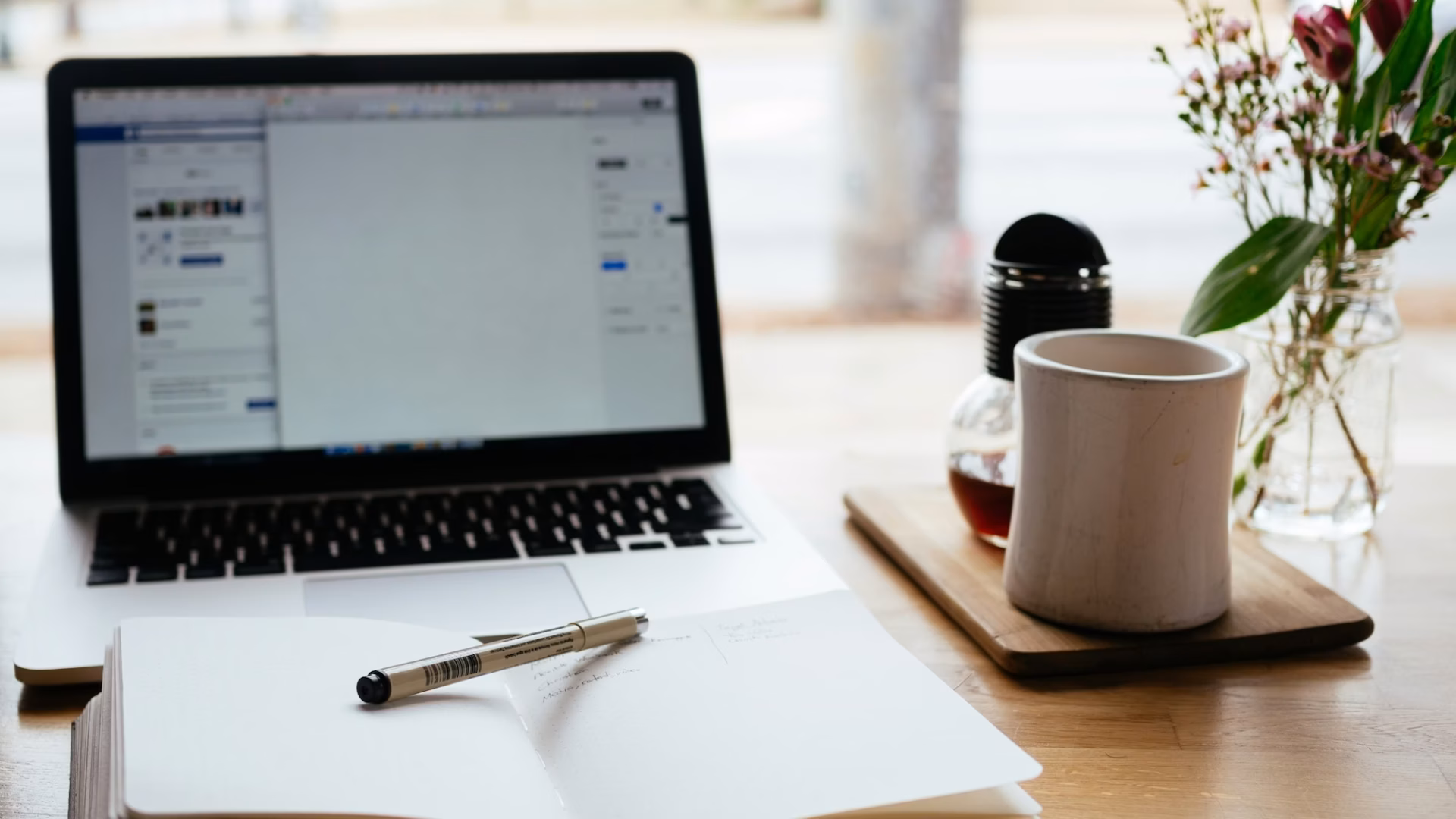 Notebook with marketing terminology written in it, with pen laid across it, sits on a desk in front of a laptop and cup of coffee