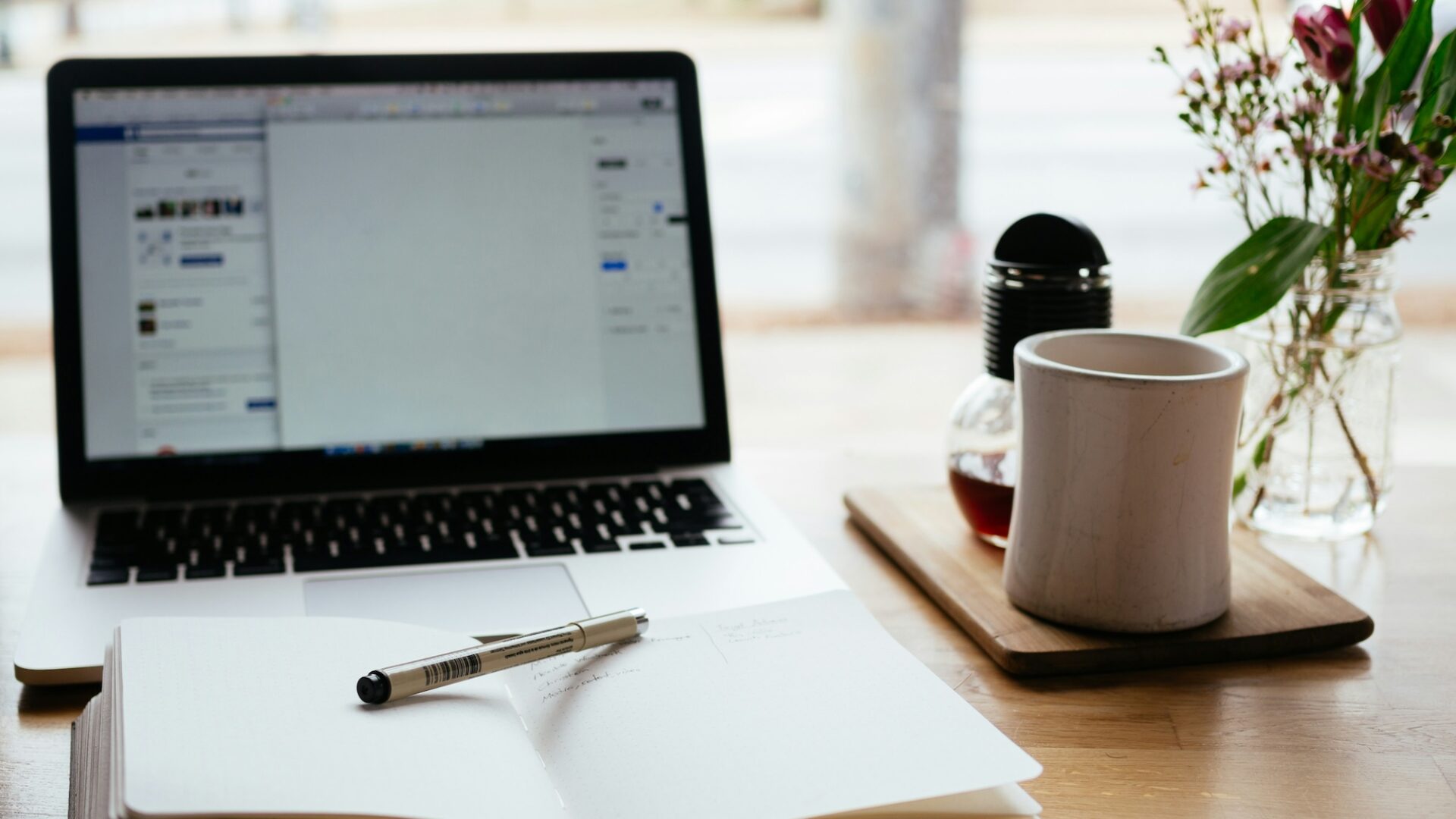 Notebook with marketing terminology written in it, with pen laid across it, sits on a desk in front of a laptop and cup of coffee