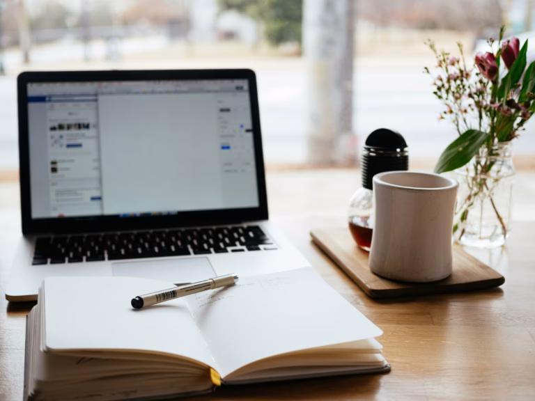 Notebook with marketing terminology written in it, with pen laid across it, sits on a desk in front of a laptop and cup of coffee