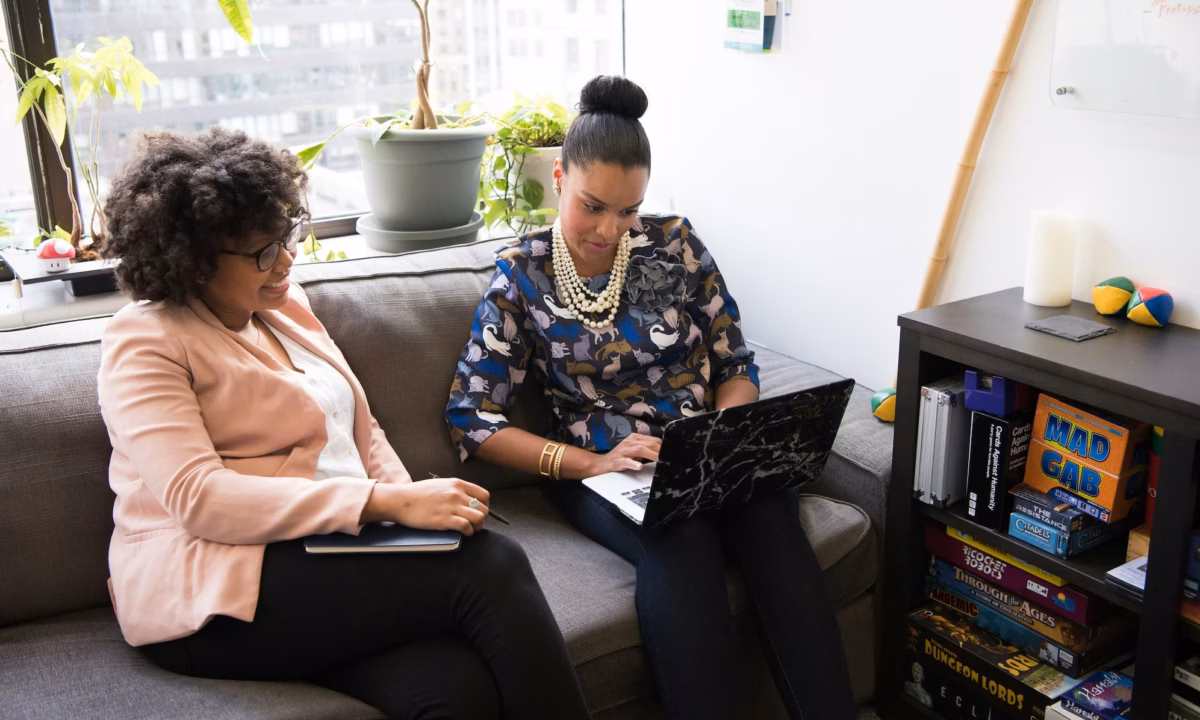 Two women sit on a couch in an office working to compile a marketing toolkit for their business