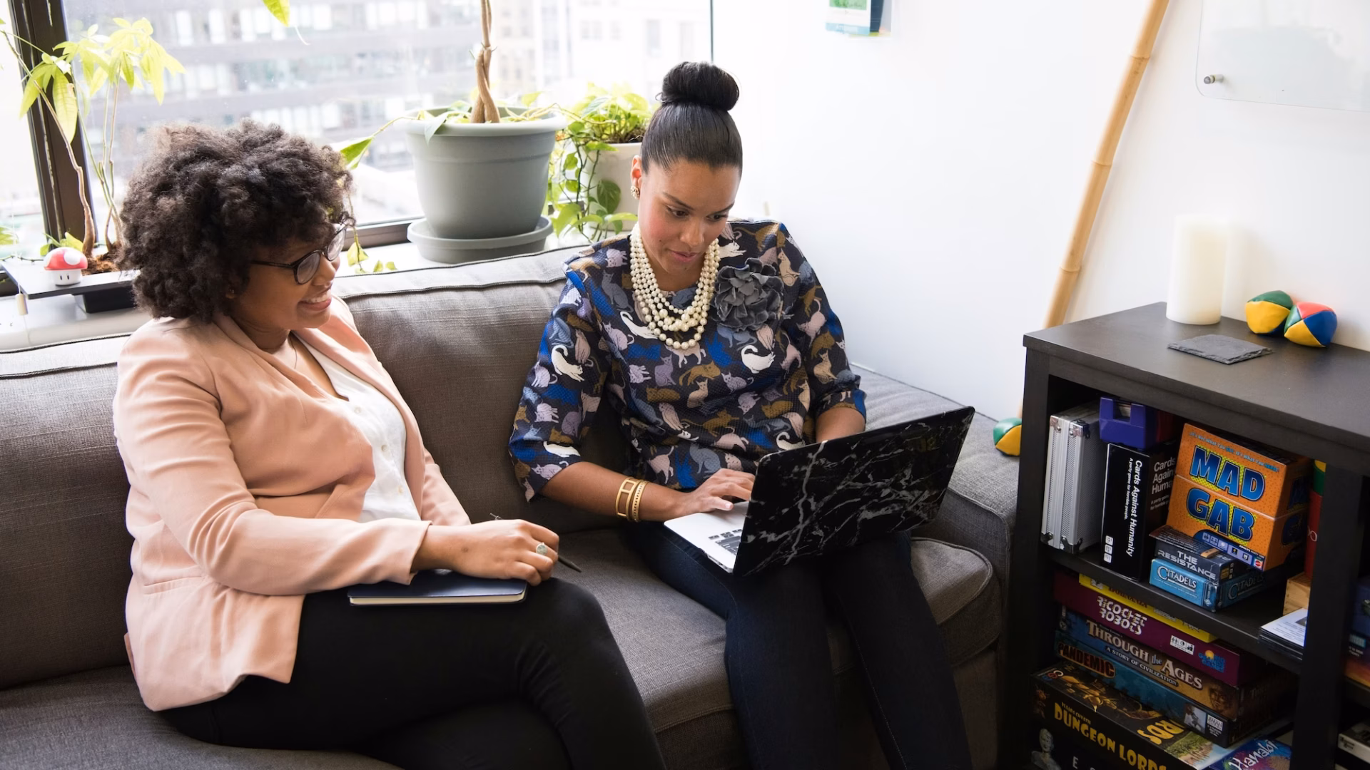 Two women sit on a couch in an office working to compile a marketing toolkit for their business