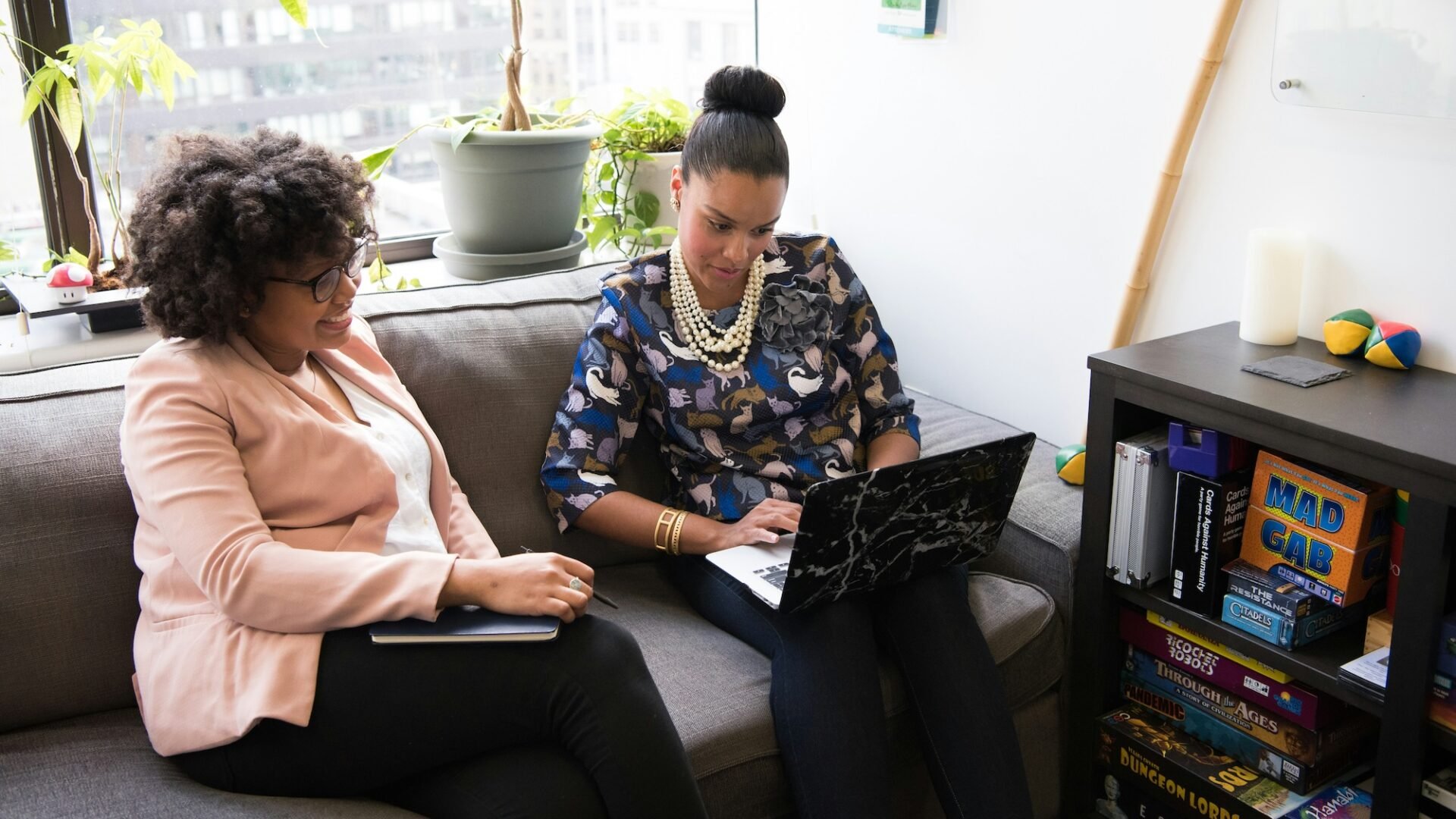 Two women sit on a couch in an office working to compile a marketing toolkit for their business