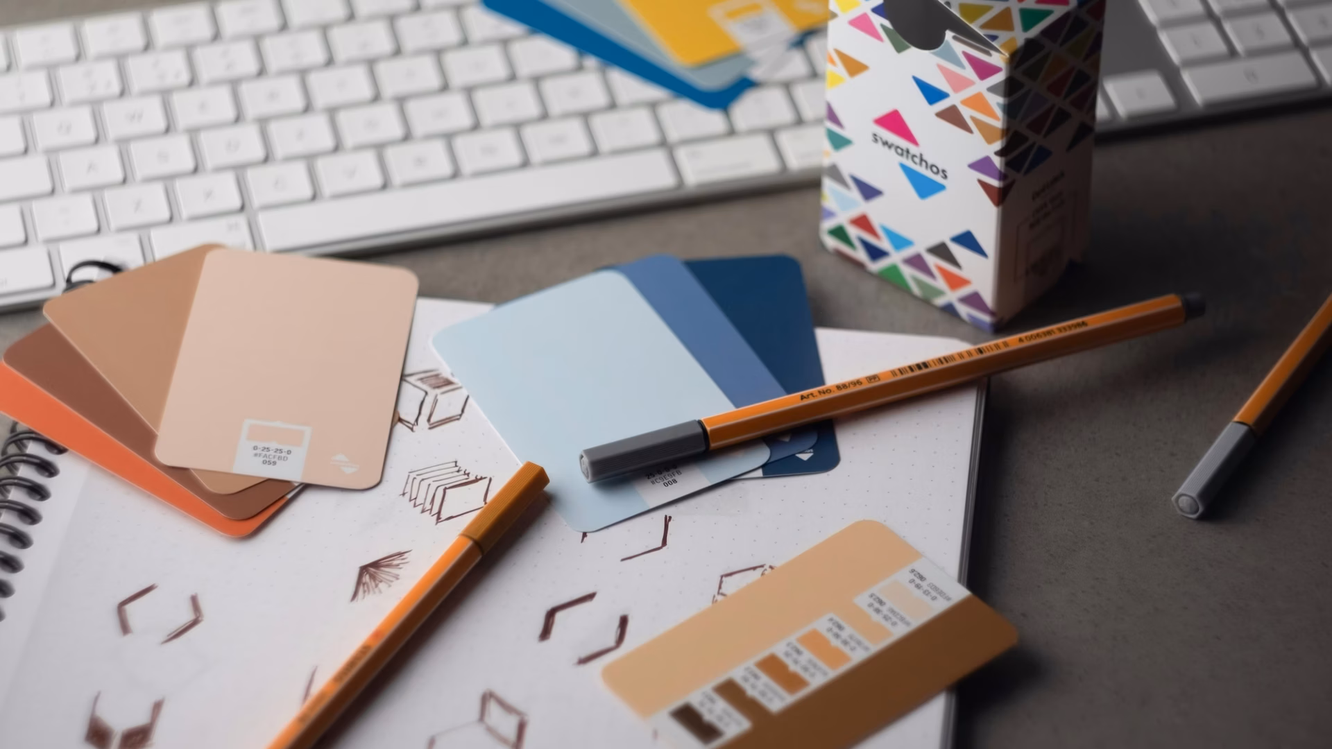 A desk with color cards, pens and sketches on it along with a keyboard, showing the journey to creating the Best real estate brands