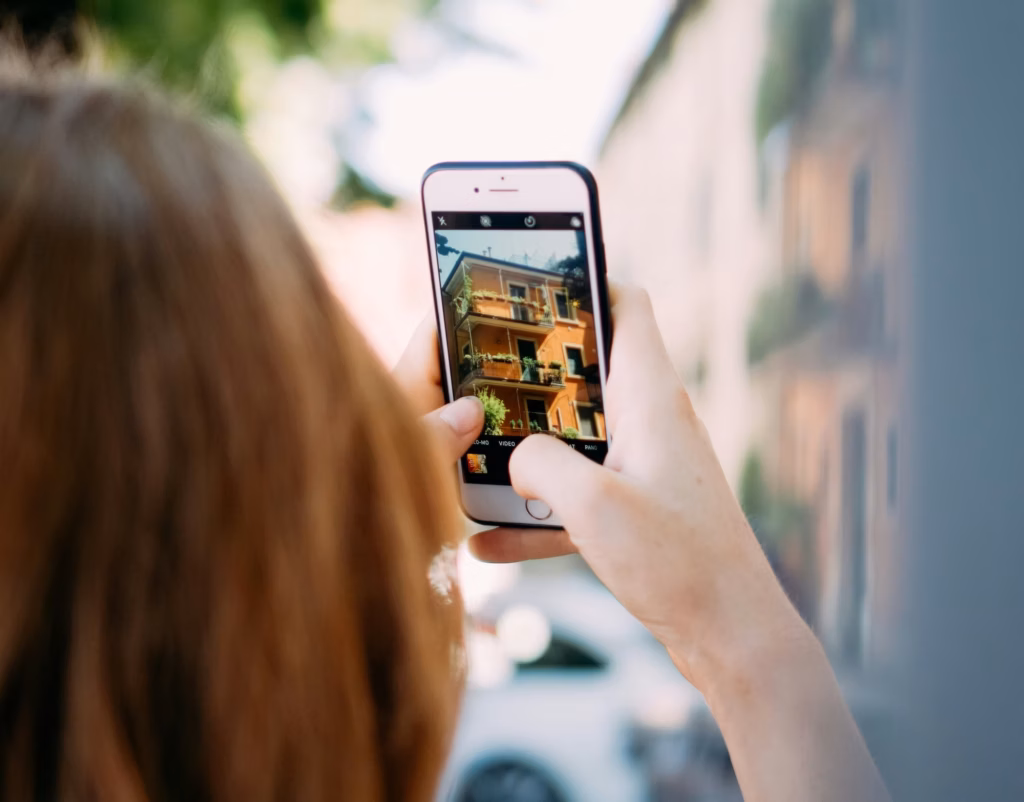 Woman holding up smartphone taking a listing photo of a small condo building for her real estate social media marketing campaign