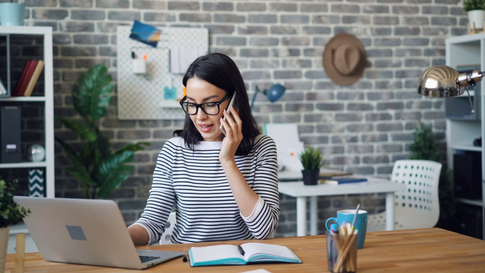 A real estate agent sits at a desk in front of a laptop on her phone, trying out real estate lead generation ideas to increase business