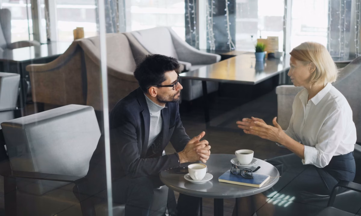 A real estate agent sits down with a prospective client at a coffee shop, explaining how Luxury Presence boosts her success rate in transactions