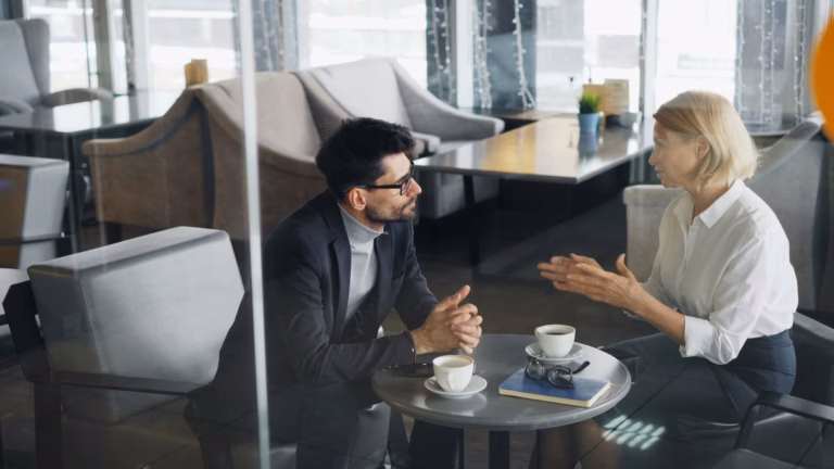 A real estate agent sits down with a prospective client at a coffee shop, explaining how Luxury Presence boosts her success rate in transactions