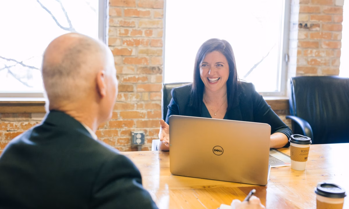 An agent meets with a prospect at a wooden office table as a result of writing and sending real estate email to clients