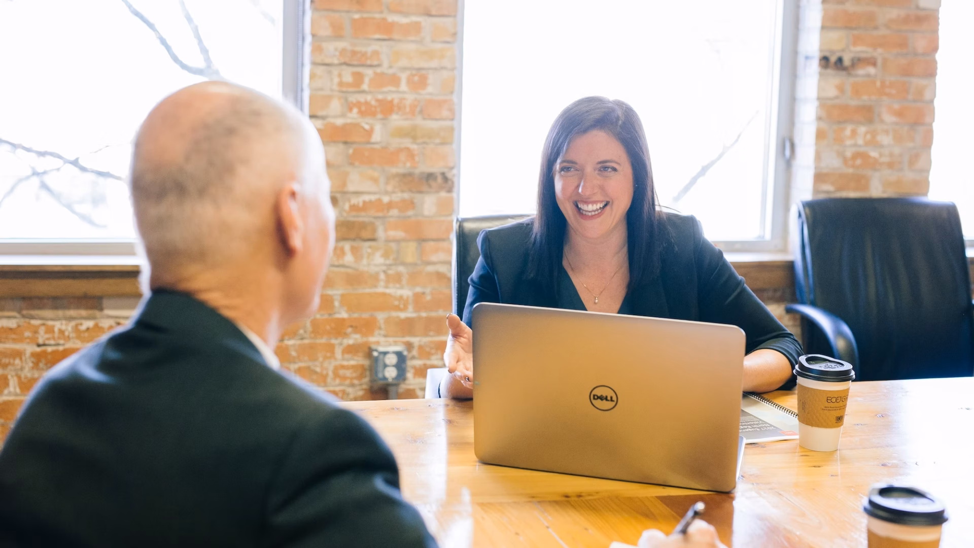 An agent meets with a prospect at a wooden office table as a result of writing and sending real estate email to clients