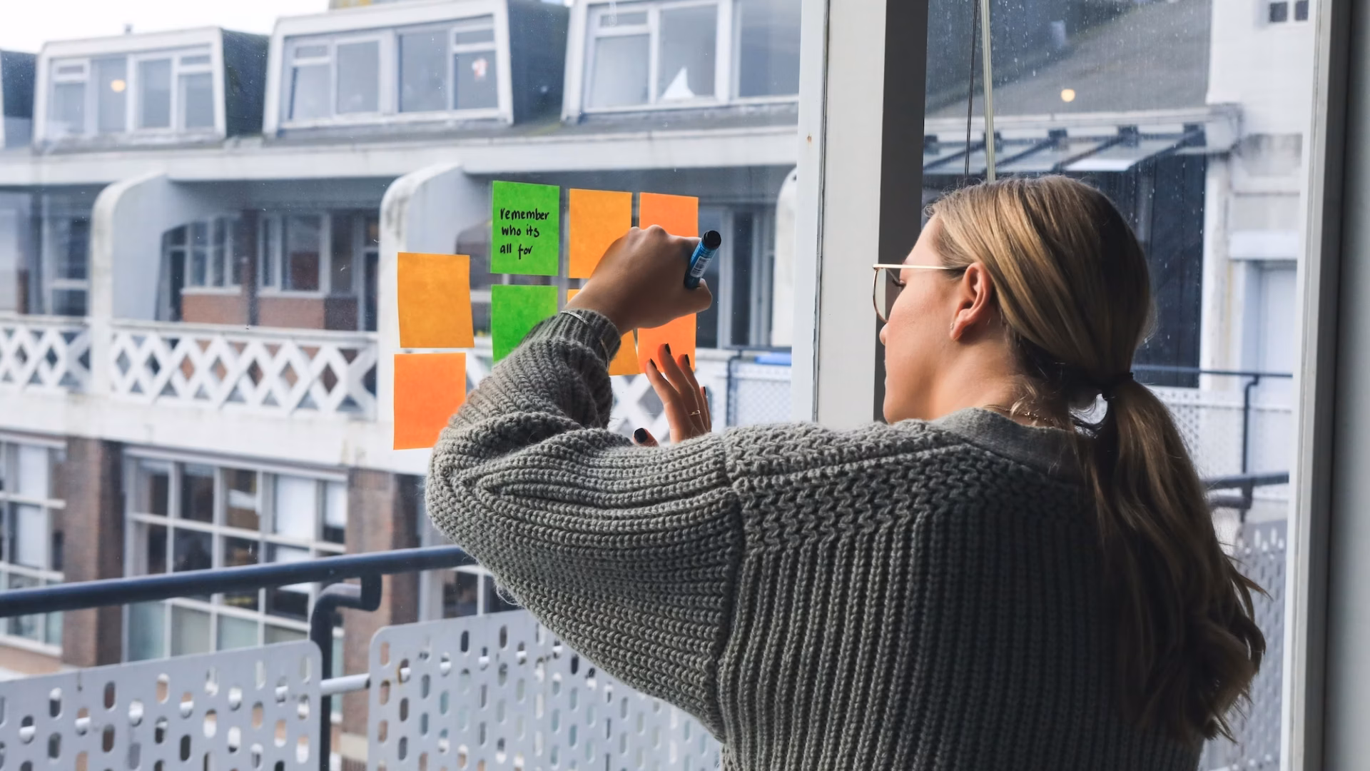 An agent writes down real estate newsletter ideas on post-it notes on a sliding glass door overlooking an apartment complex