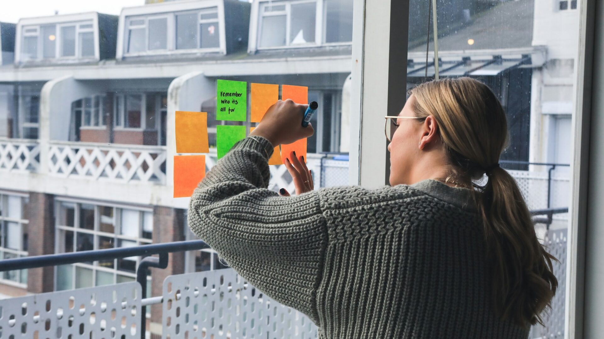 An agent writes down real estate newsletter ideas on post-it notes on a sliding glass door overlooking an apartment complex