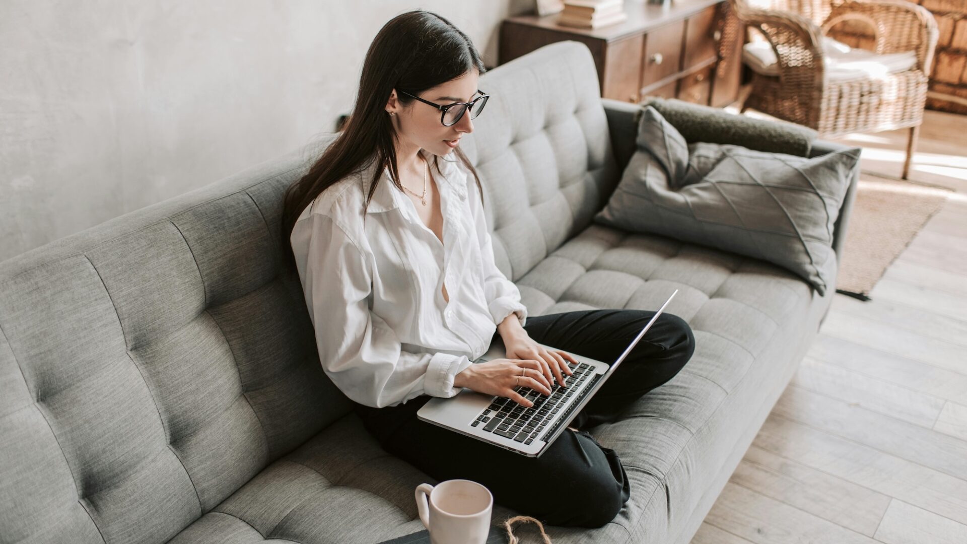 A real estate agent sits crosslegged on a grey couch, typing out a drip email marketing real estate campaign