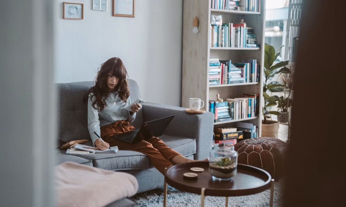 Agent sitting on a couch with a laptop and notebook, working on personalizing her real estate drip campaign templates