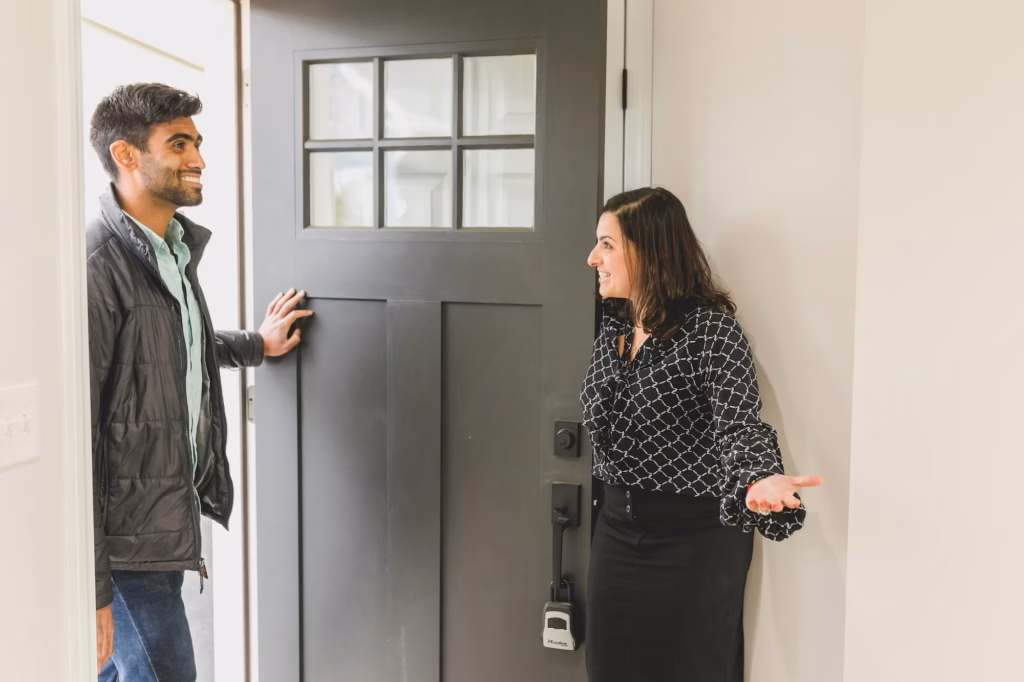 An agent opens the door to her real estate open house, greeting an attendee and potential homebuyer